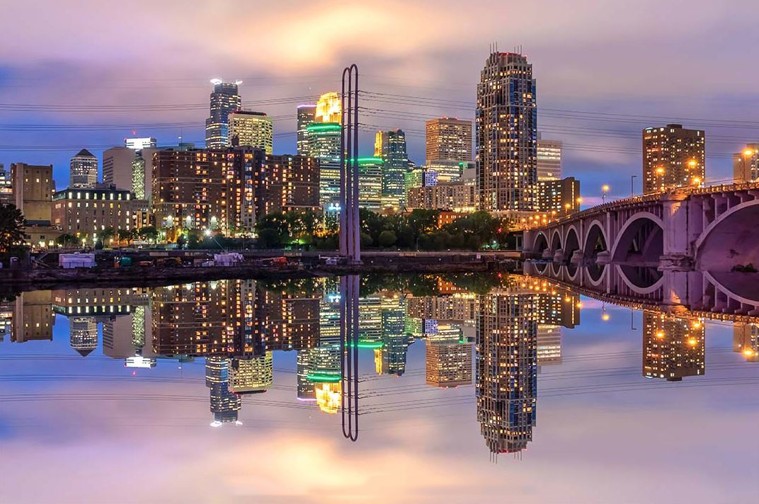 Skyline lights reflecting across calm water under mist